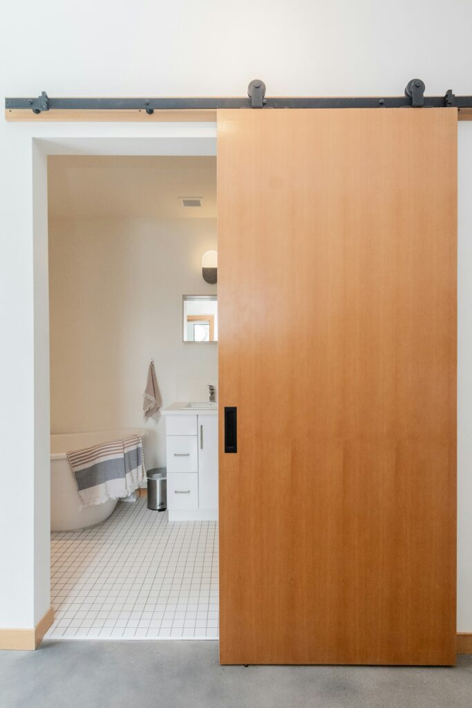 Wooden sliding door on a visible rail by a bathroom, inspiration for custom doors