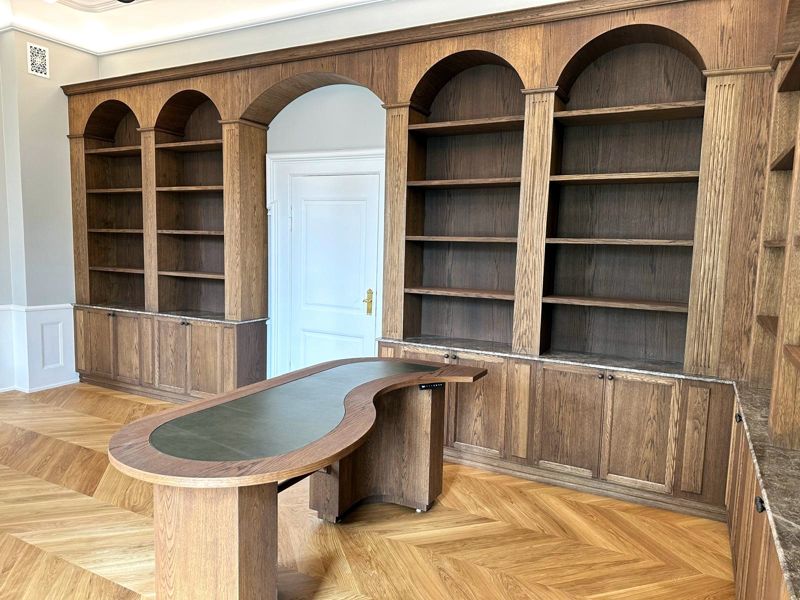 Bookcase wall in smoked oak with arches and an oval desk with leather top