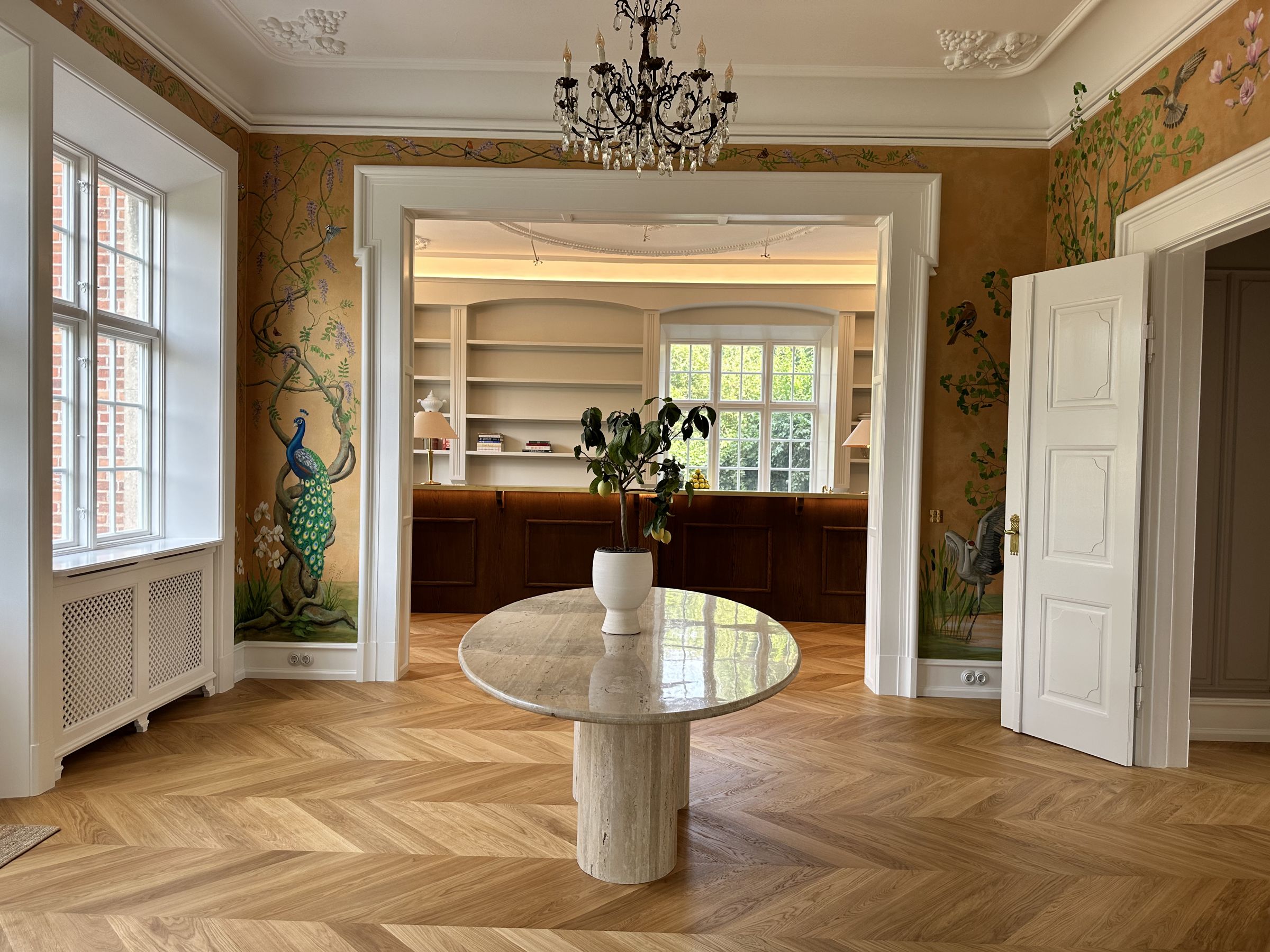Stately living room in a villa in Carlsberg City with a round travertine table, oak herringbone parquet and a built in shelving wall with an oak bench